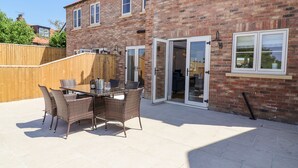 A patio with a table and chairs, a wooden fence, and a brick building with a sliding glass door. - Fishermans Lodge (York)
