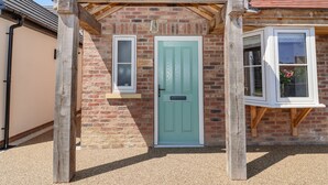 A brick building with a green door, a wooden porch, and a window with a white frame. - Fishermans Lodge (York)