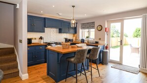 A modern kitchen with blue cabinets, a wooden island, and a dining area with bar stools. - Fishermans Lodge (York)
