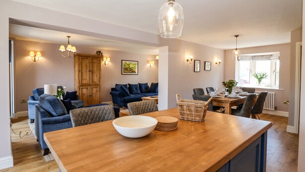 A modern kitchen with a wooden island, blue upholstered seating, and pendant lighting. - Fishermans Lodge (York)