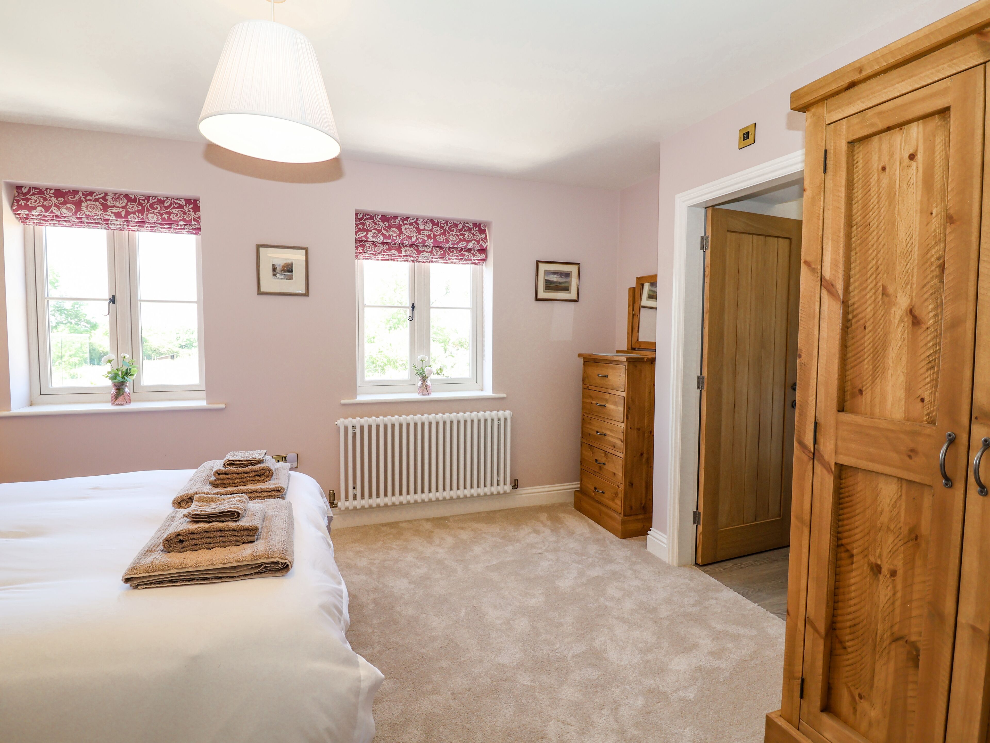 A bedroom with a bed, a dresser, a radiator, and two windows with curtains.