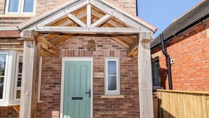Un bâtiment en briques avec une porte verte, un porche en bois et une petite fenêtre.