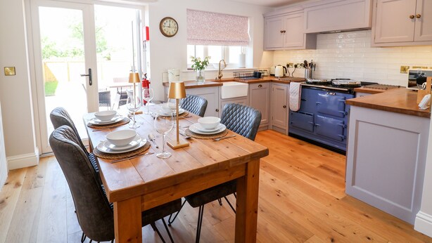 Une cuisine moderne avec des meubles en bois, une table à manger pour quatre personnes et une grande fenêtre qui laisse entrer la lumière naturelle.