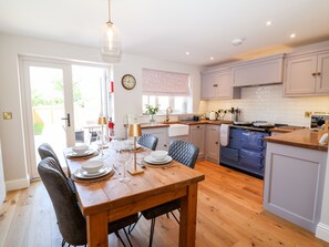 A modern kitchen with wooden cabinetry, a dining table set for four, and a large window providing natural light. - Keepers Cottage (York)