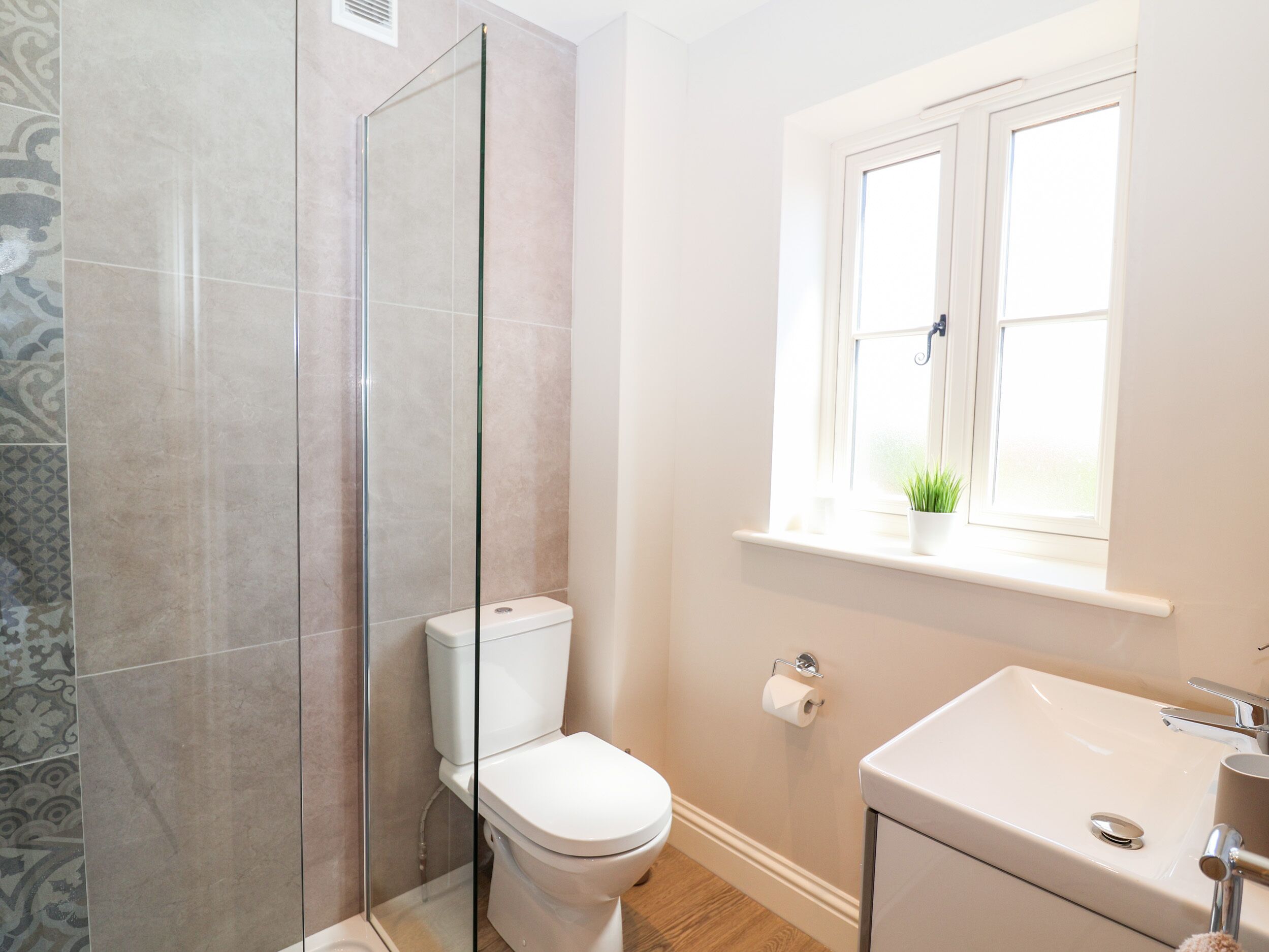 A bathroom with a glass shower enclosure, a toilet, a sink, and a window with a plant on the windowsill.