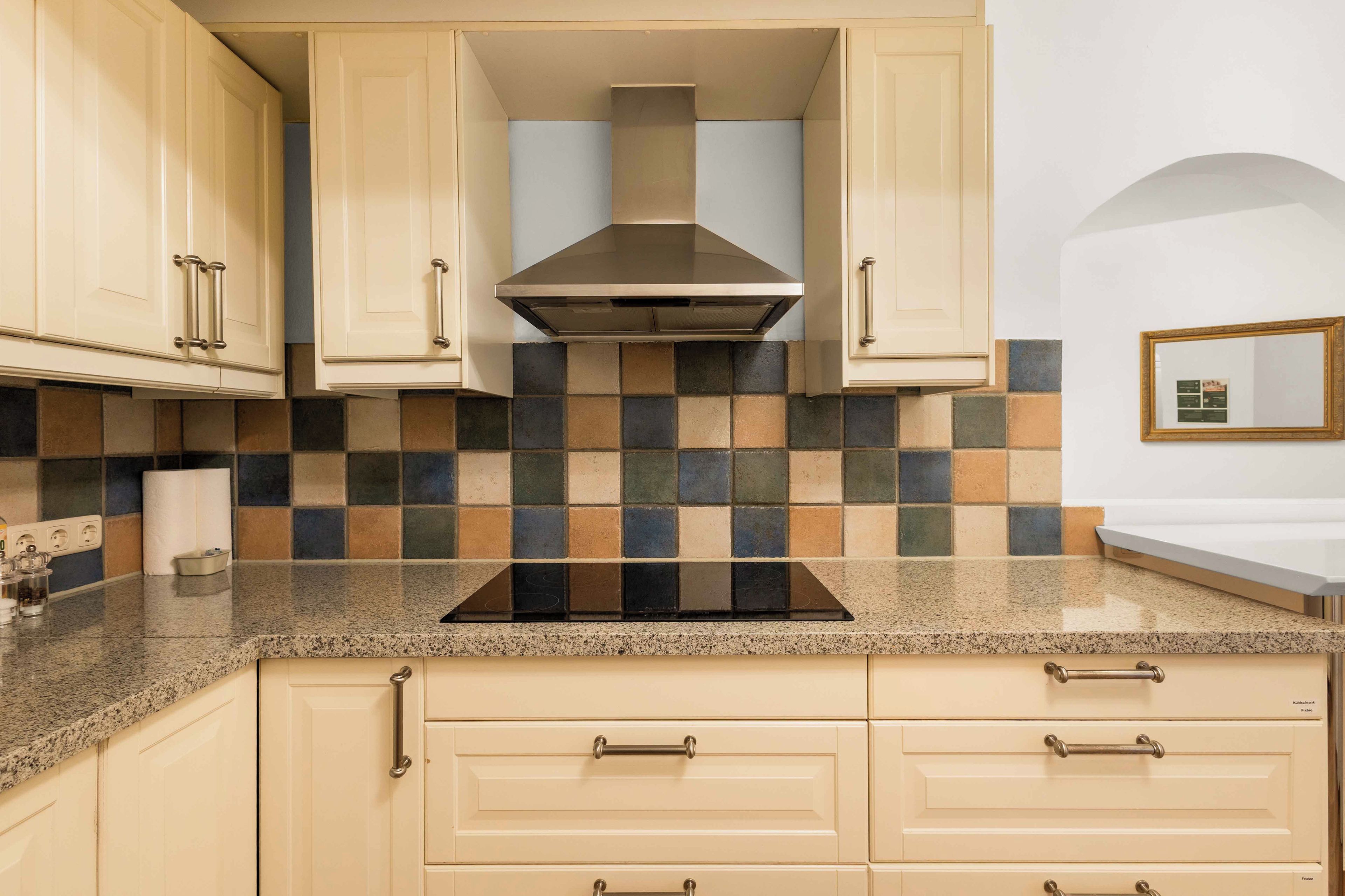 A kitchen with beige cabinets, a black stove top, and a tiled backsplash.