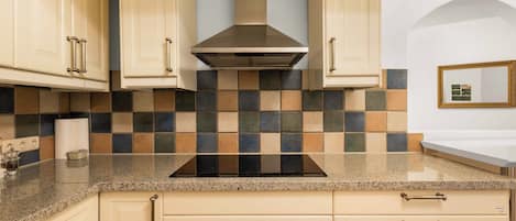 Una cocina con armarios color beige, una placa de cocina negra y un salpicadero de azulejos.