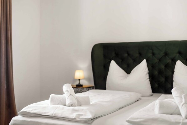 A neatly made bed with white linens and towels, a green upholstered headboard, and a bedside table with a lamp. - Königlicher Aufenthalt 10 Minuten zu Fuß zum See (Prien am Chiemsee)