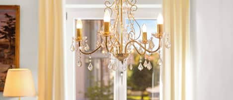 A chandelier with multiple arms and crystal decorations, a window with curtains, and a lamp on the left.