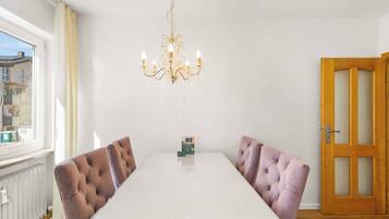 Ein Esszimmer mit einem weißen Tisch, vier gepolsterten Stühlen, einer Kandelaber und einer Holztür.
