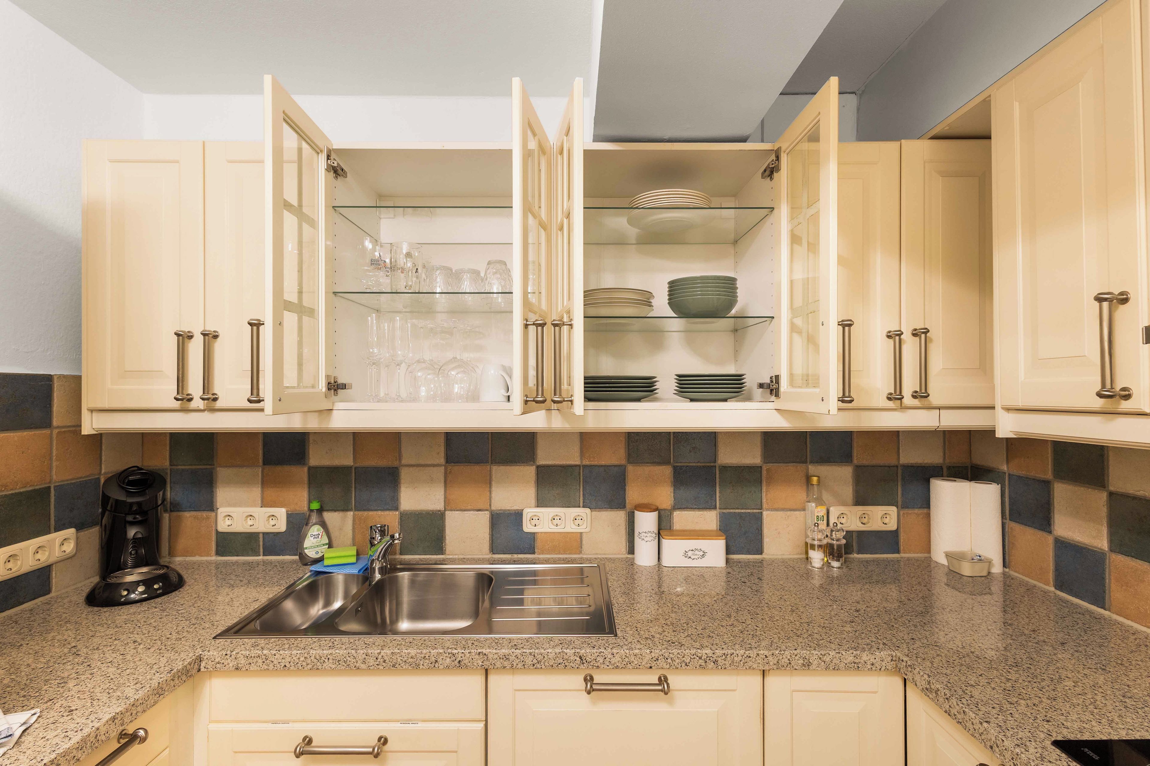 A kitchen with open cabinets, a granite countertop, and a stainless steel sink.