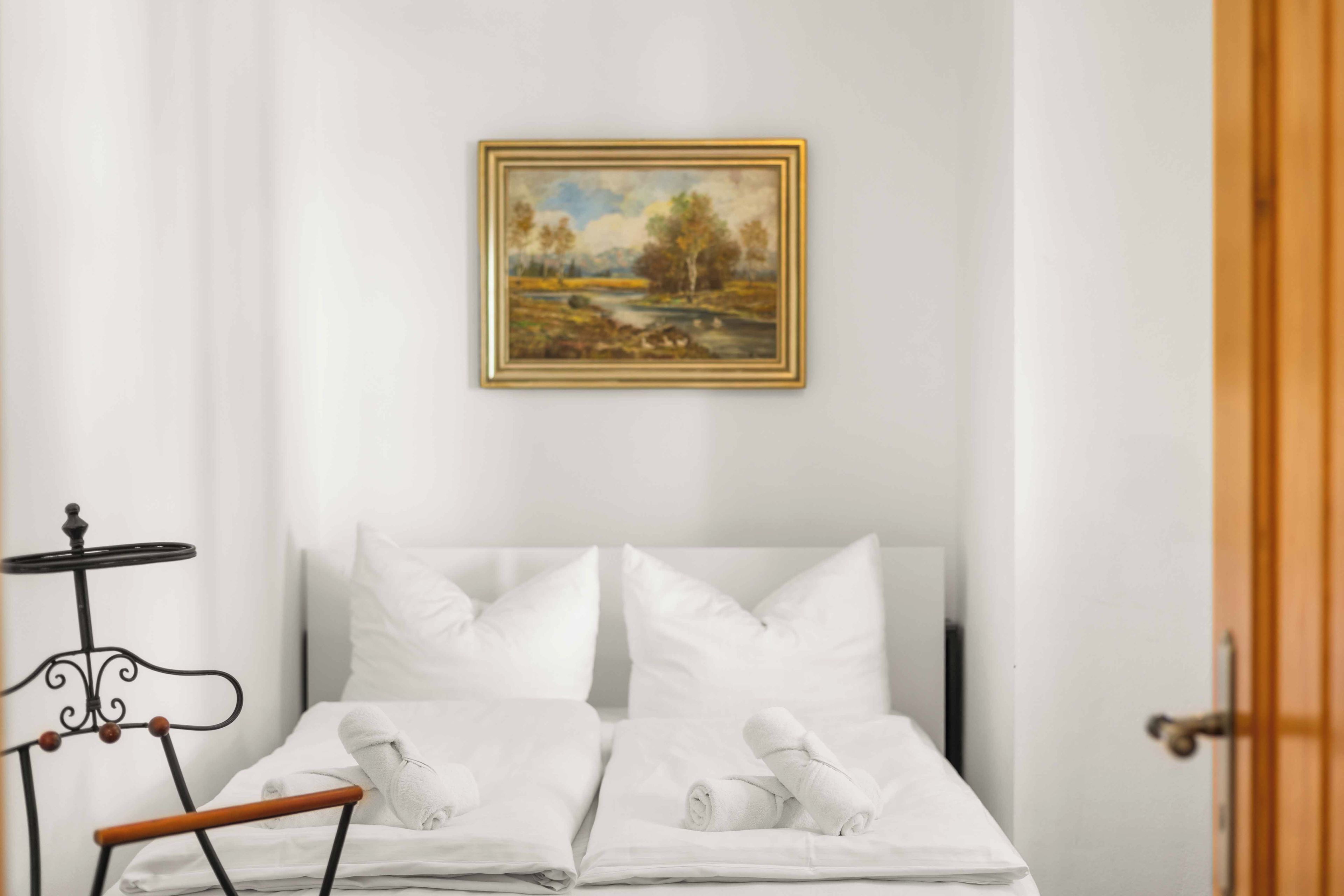Ein Hotelzimmer mit Bett, Kissen, einem kleinen Tisch und einem Gemälde an der Wand.