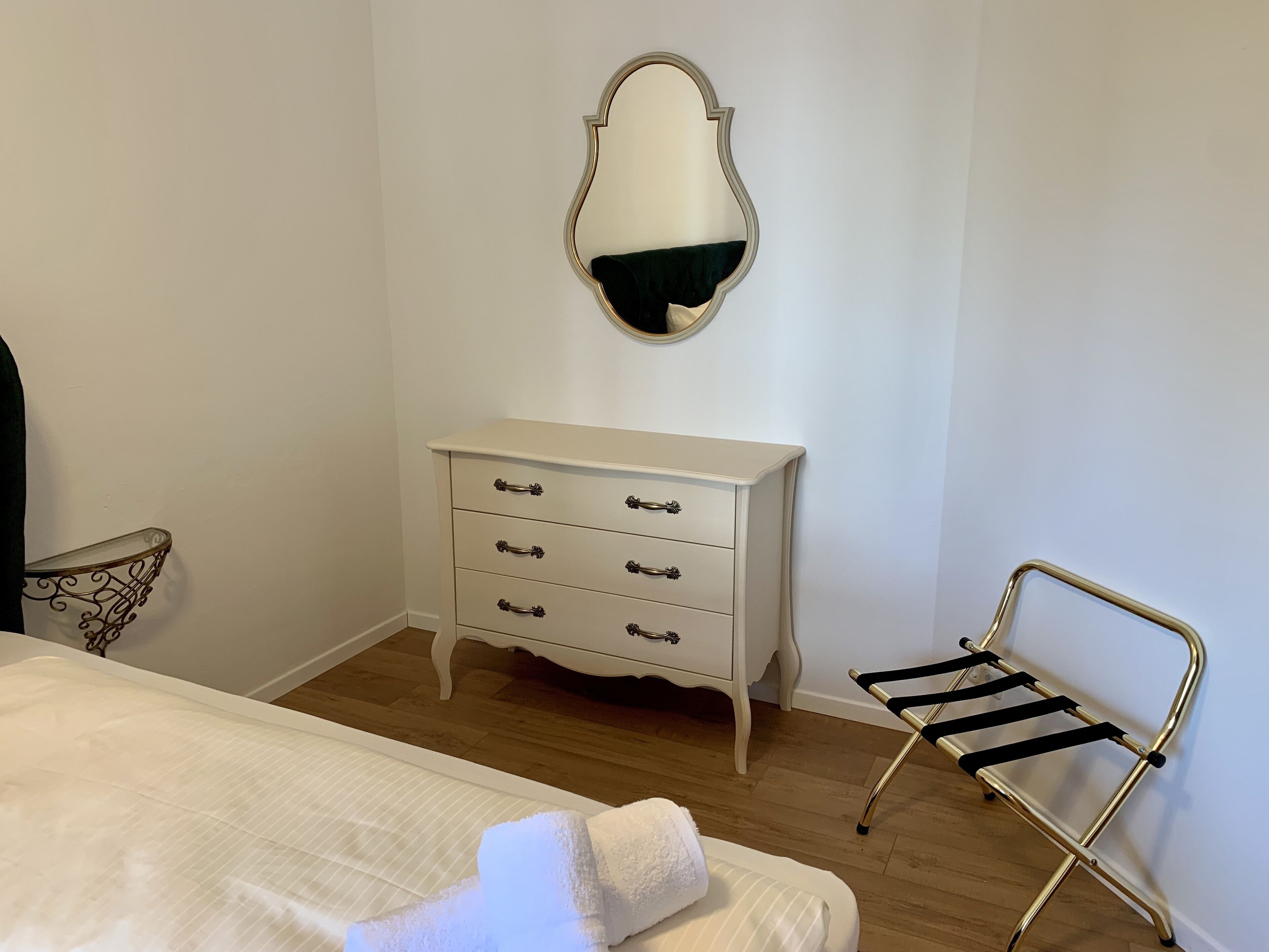 Ein Schlafzimmer mit einem Bett, einer weißen Kommode mit Schubladen, einem Spiegel und einem Metallstuhl.