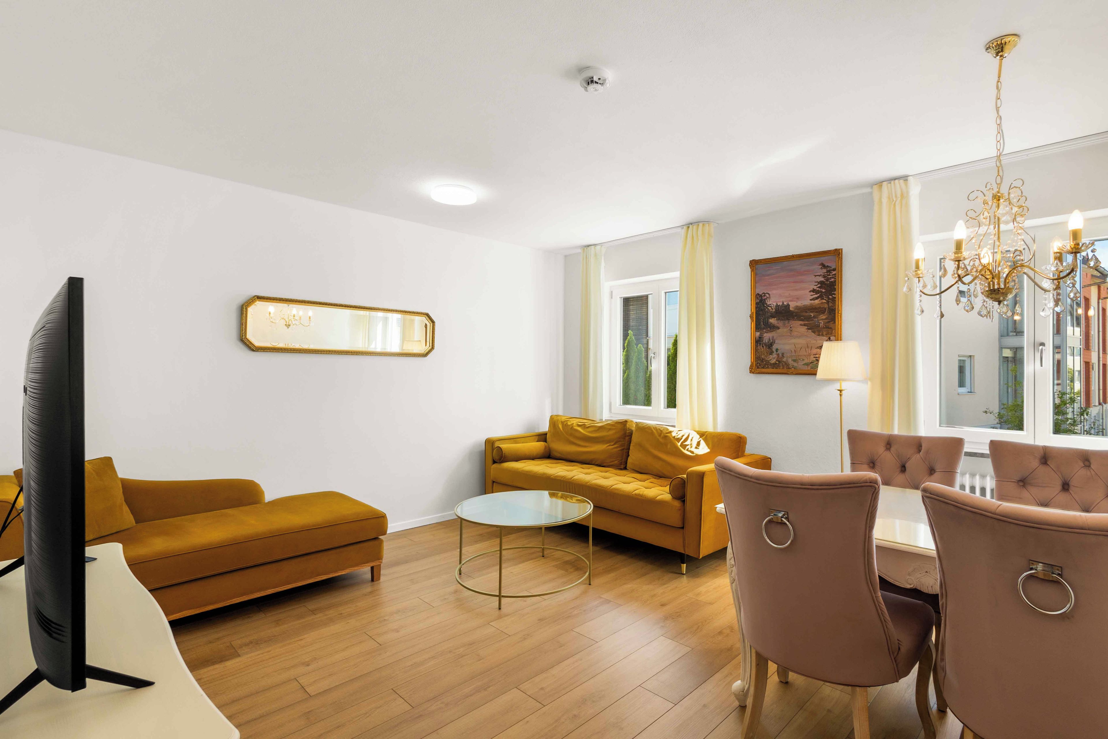 Ein modernes Wohnzimmer mit Sofa, Couchtisch, Fernseher und einem Essbereich mit Stühlen.
