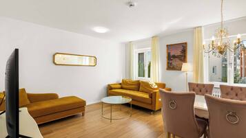 Ein modernes Wohnzimmer mit Sofa, Couchtisch, Fernseher und einem Essbereich mit Stühlen.