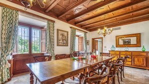 Ein Esszimmer mit Holztisch und Stühlen, einer Chandelierleuchtre und Blick ins Freie durch große Fenster.