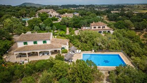Eine großzügige Villa mit Swimmingpool, umgeben von üppiger Vegetation und einer hügeligen Landschaft im Hintergrund.