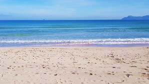 Ein Strand mit Fußabdrücken, die zum Wasser führen, ein klarer Himmel und ferne Berge.
