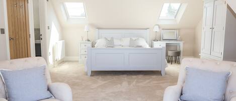 A bedroom with a large bed, two armchairs, a desk, and a wardrobe.