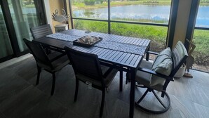 A dining area with a table and chairs, large windows with a view of a lake and trees, and a ceiling light. - Resort Style 55+ Community! Includes golf cart and amazing sunset views! (Fort Myers)