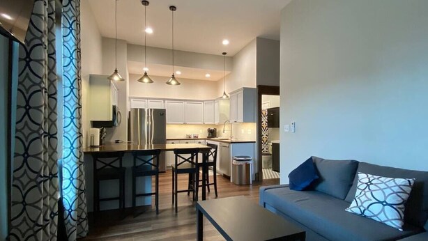 A modern kitchen with a central island, pendant lighting, and a dining area with a sofa and coffee table. - Copperfield- Unit 2 - 1 Bedroom Luxury Suite - King (Centralia)