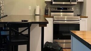 A compact kitchen with white cabinets, a microwave, an oven, and a dining table with chairs. - Copperfield- Unit 2 - 1 Bedroom Luxury Suite - King (Centralia)