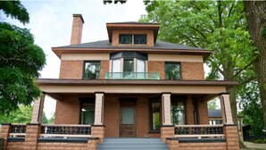 A two-story brick house with a front porch, a balcony, and a chimney. - Copperfield- Unit 2 - 1 Bedroom Luxury Suite - King (Centralia)