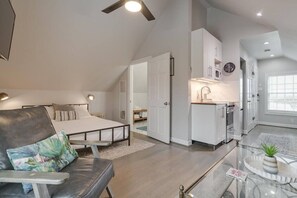 A bedroom with a bed, a desk, and a chair. There is a kitchenette with a microwave, a sink, and cabinets.