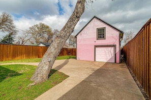 A pink single-story building with a garage, surrounded by a wooden fence and a tree.