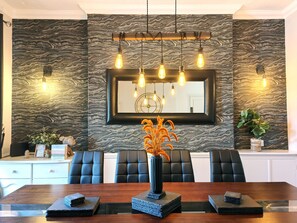 A dining area with a marble-patterned wall, a wooden dining table, black upholstered chairs, a vase with dried flowers, and a hanging light fixture. - Squirrel Lodge (Keswick)