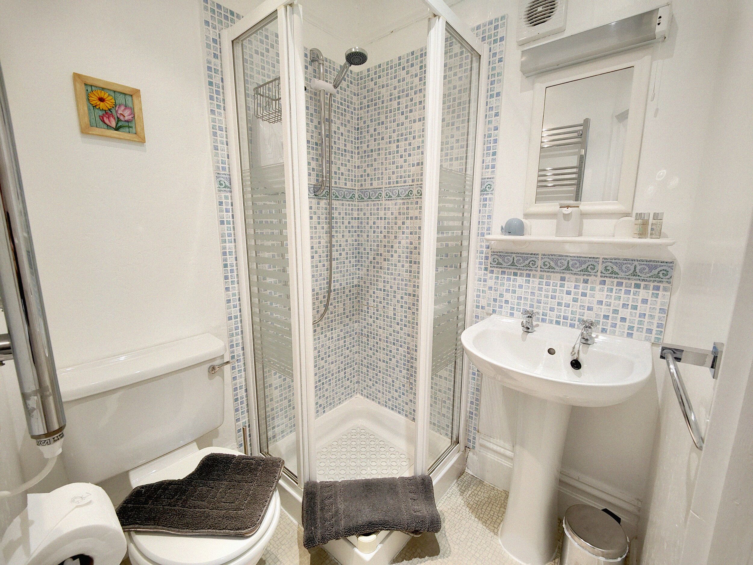 Een badkamer met douche, toilet, wastafel en een klein decoratief object aan de muur.