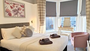 A hotel room with a large bed, a desk, a chair, and a window with curtains. - Squirrel Lodge (Keswick)