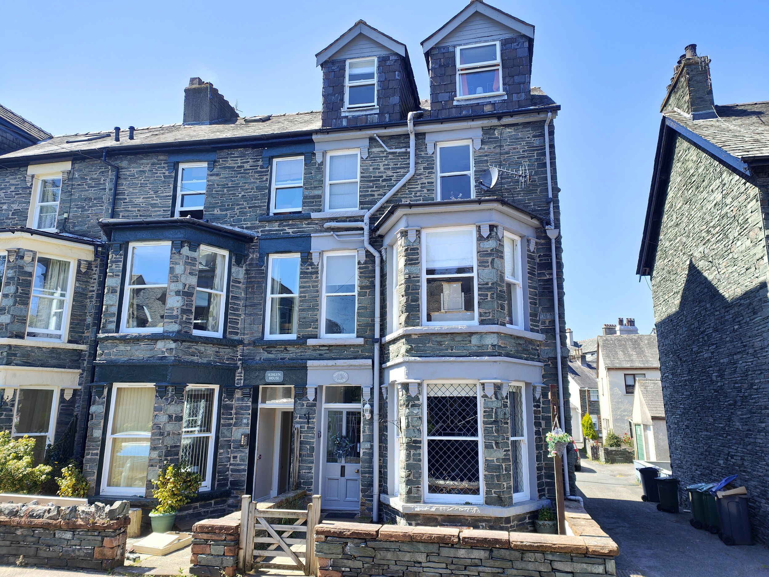 A stone-built two-story house with a bay window, a front door, and a small porch area.