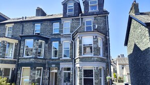 A stone-built two-story house with a bay window, a front door, and a small porch area. - Squirrel Lodge (Keswick)
