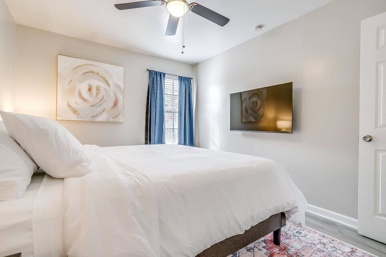 Ein Schlafzimmer mit einem Bett, einem Deckenventilator, einem Fenster mit Vorhängen und zwei an der Wand befestigten Kunstwerken.