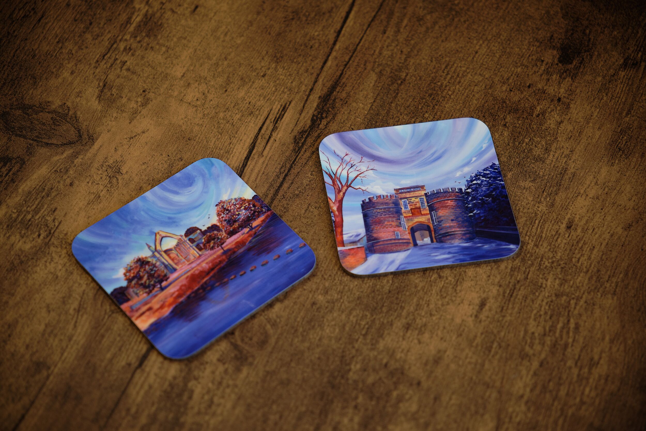 Deux sets de table carrés, ornés d’images représentant un pont et un château, posés sur une table en bois.