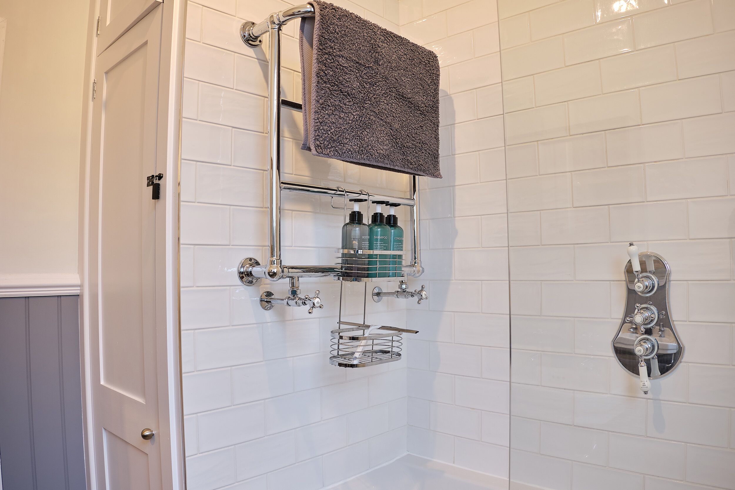A bathroom with white tiled walls, a shower with a handheld showerhead, and a towel rack with a dark towel.
