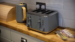 A kitchen with a grey toaster, a wooden cutting board, and a kettle. - Flat Cap Cottage (Skipton)
