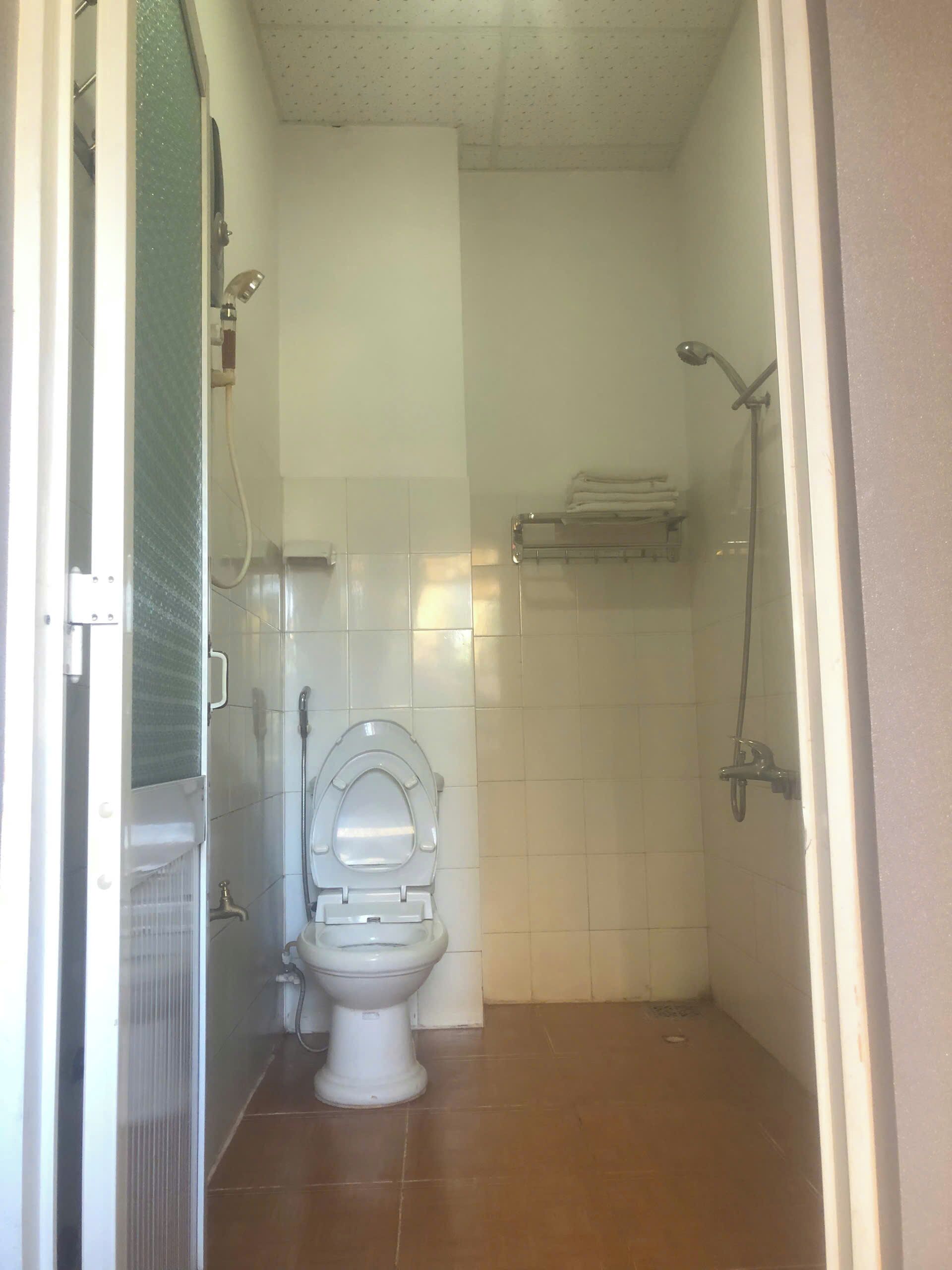 A small, tiled bathroom with a toilet, a shower, and a towel rack.