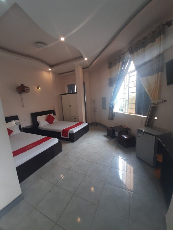 A hotel room with two beds, a small kitchenette, a wardrobe, and a window with curtains.
