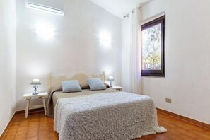 Una camera da letto con un letto, due comodini, una finestra e un pavimento in legno.