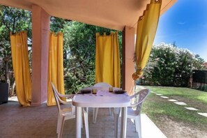 Patio esterno con tavolo e sedie, circondato da tende gialle, riparato da una struttura.