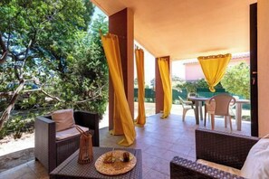 Una veranda esterna con mobili in vimini, un tavolo con tovaglia tessuta e tende gialle.