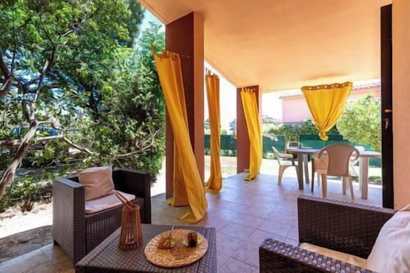 An outdoor patio with wicker furniture, a table with a woven placemat, and yellow curtains.