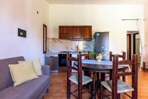 A living room with a sofa, a dining table with chairs, a kitchen area with cabinets, and a refrigerator. - 100 meters from the beach! Wonderful Villa in Costa Rei (Costa Rei)