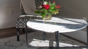 Una mesa redonda de mármol con un centro de mesa floral, un sofá estampado y un cuadro en la pared.