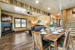 L’intérieur chaleureux d’un chalet avec une table à manger en bois, préparée pour quatre personnes, une cheminée et un coin salon confortable.