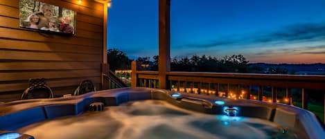A hot tub with a wooden deck and a view of a sunset.