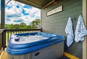 A hot tub on a wooden deck with a view of trees and a house in the background. - Fenced Yard · Stadium Theater · Hot Tub · Fire Pit· Flat Roads - Sleeps 10 (Sevierville)