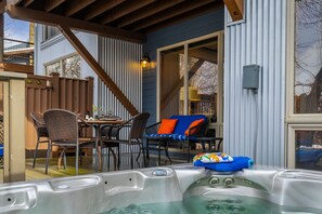 Un porche cubierto con un jacuzzi, mobiliario exterior y una escalera de madera.